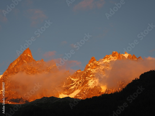 aiguilles secteur chamonix, Mont-Blanc, au coucher de soleil, avec roches orangées, nuage et ciel bleu.