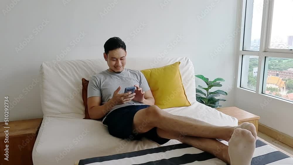 Asian man happy with the mobile application while relax on his sofa.
