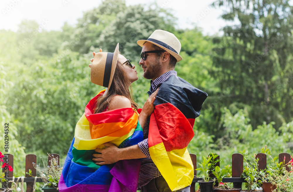 Happy heterosexual couple in hats wrapped in a German and rainbow flags. Happy heterosexual couple in hats wrapped in a German and rainbow flags.