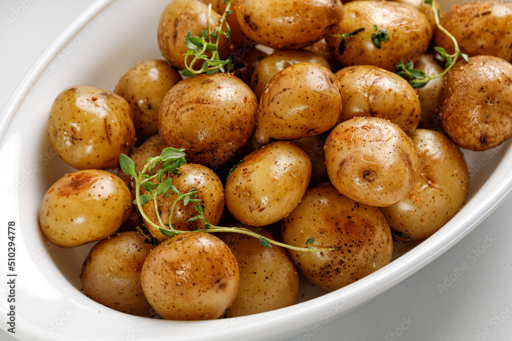 Roasted baby new young potatoes in white baked dish with thyme, close up. Roasted baby new young potatoes in white baked dish with thyme, close up.