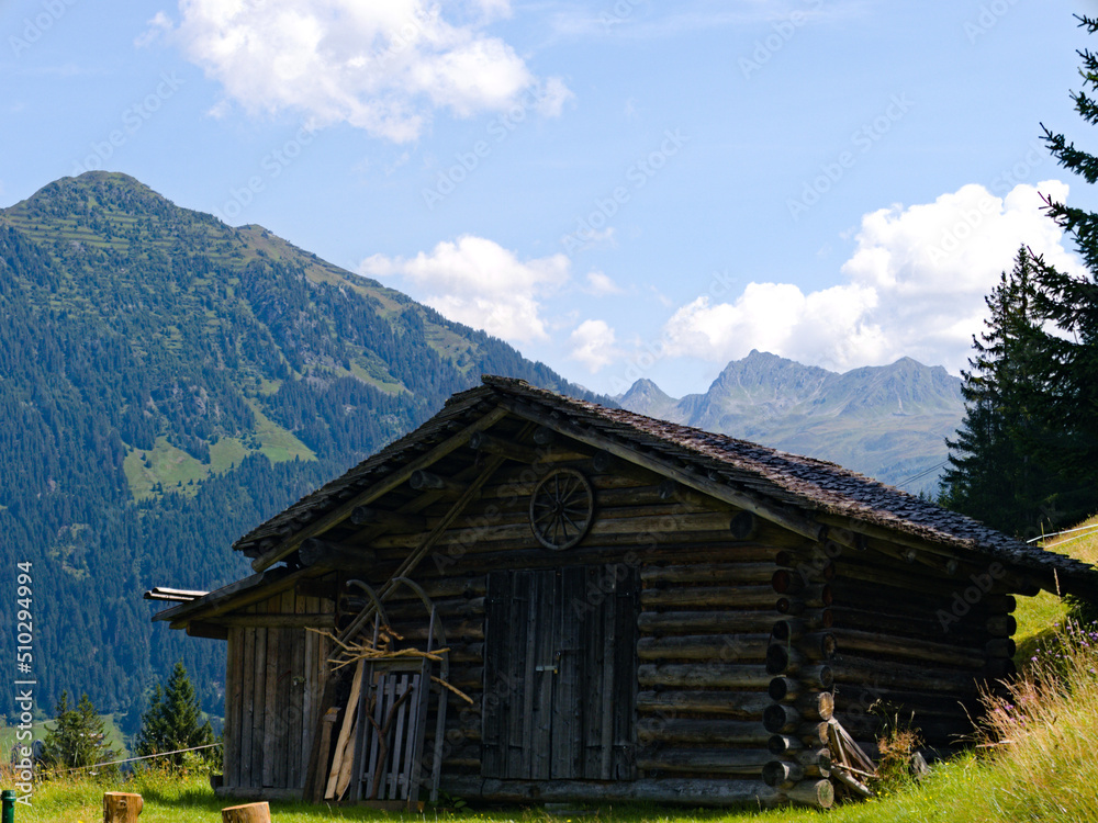 Holzhütte in den Alpen mit Bergen und blauem Himmel im Hintergrund