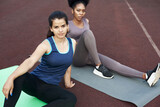 Portrait of stylish multiethnic women sitting in the stadium. Asian and african american women relaxing after workout and looking at the camera.