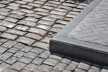 The corner of the sidewalk made of stone tiles with access to the road paved with cobblestones close-up of a clean old road on a sunny day cityscape, nobody.