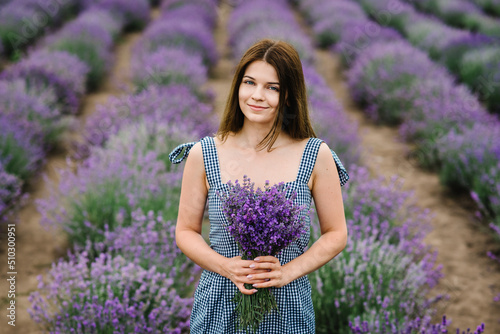 Girl in dress in a purple lavender field. A beautiful woman walk on the lavender field. Female collect lavender. Enjoy the floral glade, summer nature. Natural cosmetics and eco makeup concept.