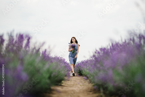 Girl holding bouquet of flowers in a purple lavender field. A beautiful woman walk on the lavender field. Female collect lavender. Enjoy the floral glade, summer nature. Natural cosmetics concept.
