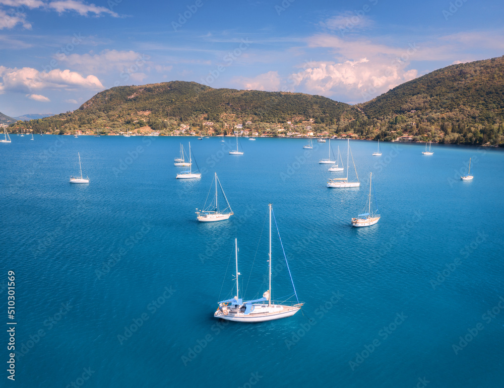 Aerial view of beautiful yachts. Boats on the sea at sunset in summer. Lefkada island, Greece. Top view of luxury yachts, sailboats, clear blue water, sky, mountain. Travel. Cruise vacation. Yachting