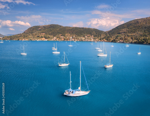Aerial view of beautiful yachts. Boats on the sea at sunset in summer. Lefkada island, Greece. Top view of luxury yachts, sailboats, clear blue water, sky, mountain. Travel. Cruise vacation. Yachting