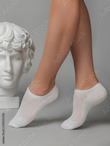 Cropped side view of a beautiful woman's legs in white socks, isolated against a gray background. Young woman walking on tiptoes. Comfortable footwear for ladies and girls. Cozy women's hosiery.