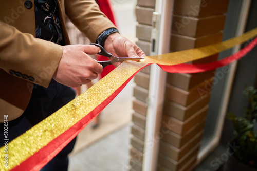 a man cuts gold and red ribbons with scissors at the grand opening