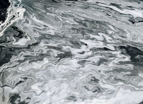 Spring pollen spread over the surface of the puddle after rain and formed abstract swirling patterns. Interesting complex natural white and black texture.