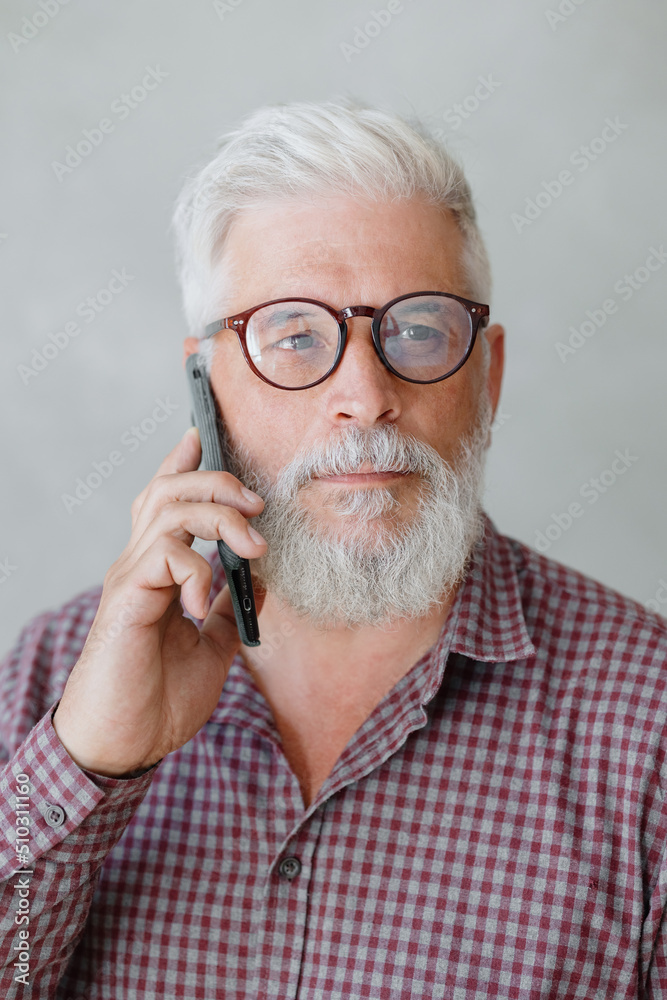 man with gray hair is working in an office on a laptop and talking on the phone. an adult male director or businessman is negotiating on an online webcam. business and finance of a male lawyer or