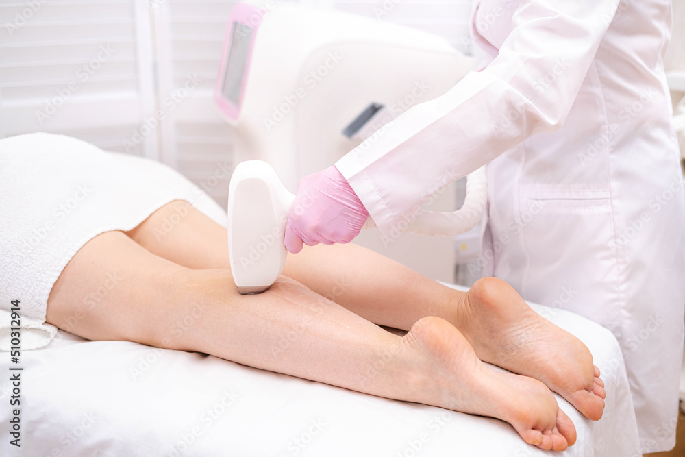Fototapeta premium Diode laser hair removal, Beautician removes hair on beautiful female legs, Hair removal for smooth skin, laser procedure at beauty studio or clinic, Body care epilation treatment.