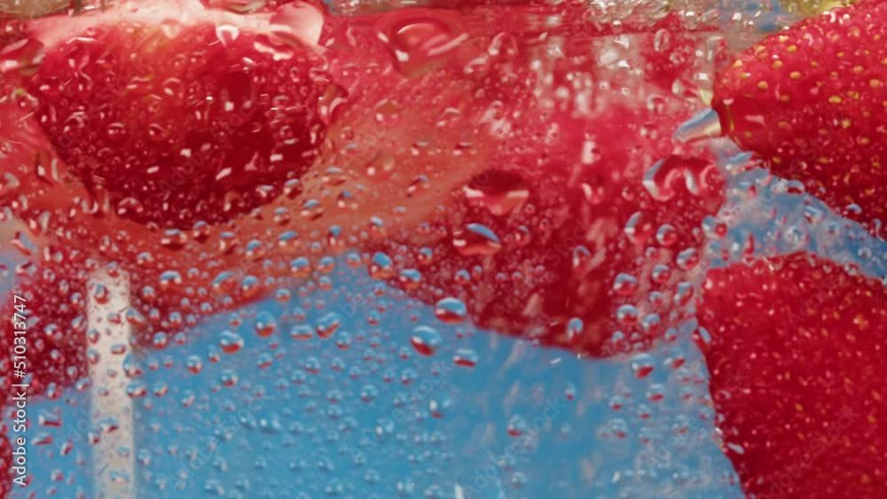 Cooking strawberry sweet cocktail, cold lemonade with red berries, carbonated water with floating fruits on blue background. Cooking strawberry sweet cocktail, cold lemonade with red berries, carbonated water with floating fruits on blue background.