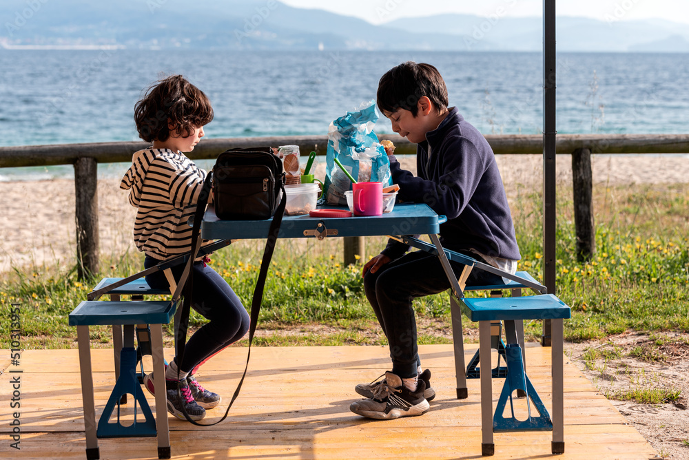 two children having breakfast at a blue table on the beach