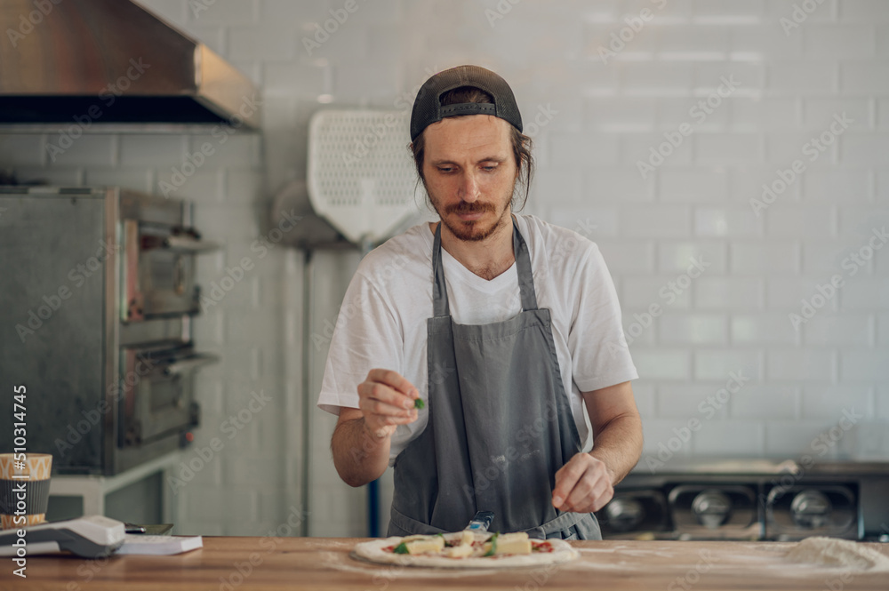 Man worker in a pizza place placing ingredients on pizza dough Man worker in a pizza place placing ingredients on pizza dough