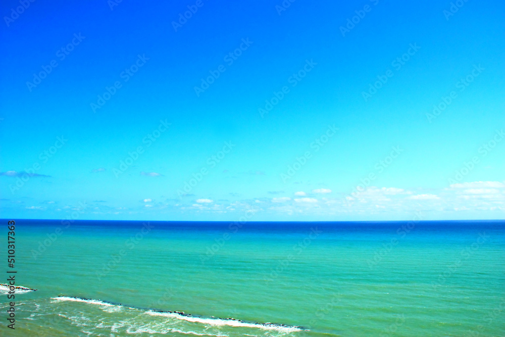 Beautiful view of the Adriatic Coast in Ortona with serene azure sky and colorful sea ranging from cyan to deep blue with pure white foam fuming behind rocks on a sunny summer day