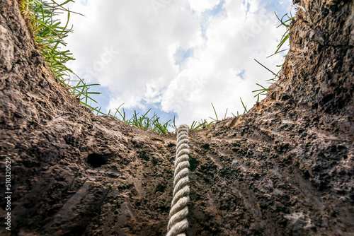 Looking up from hole in ground with rope. Lifeline, debt, mental health help concept.  photo