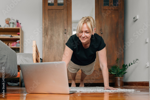 mature woman at home doing sport yoga on the floor with laptop online classes  photo