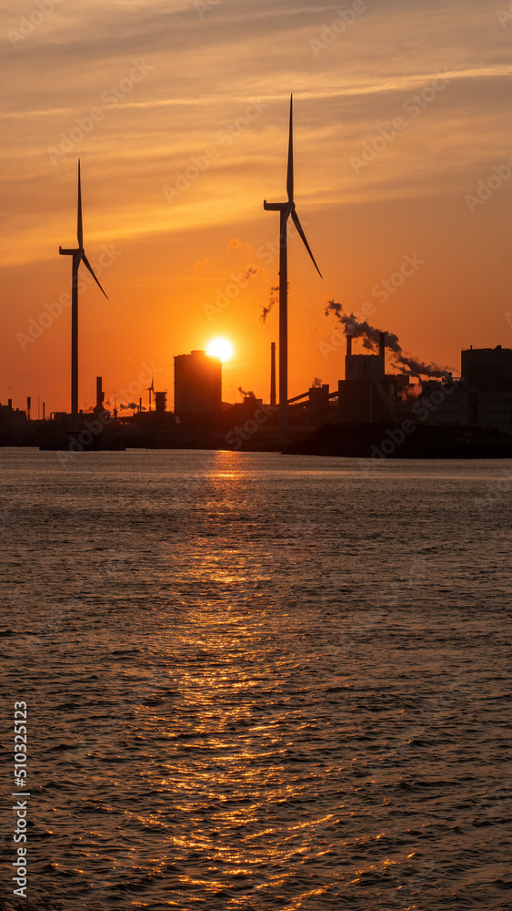 Silhouette of wind turbines in industrial area by the sea on sunset