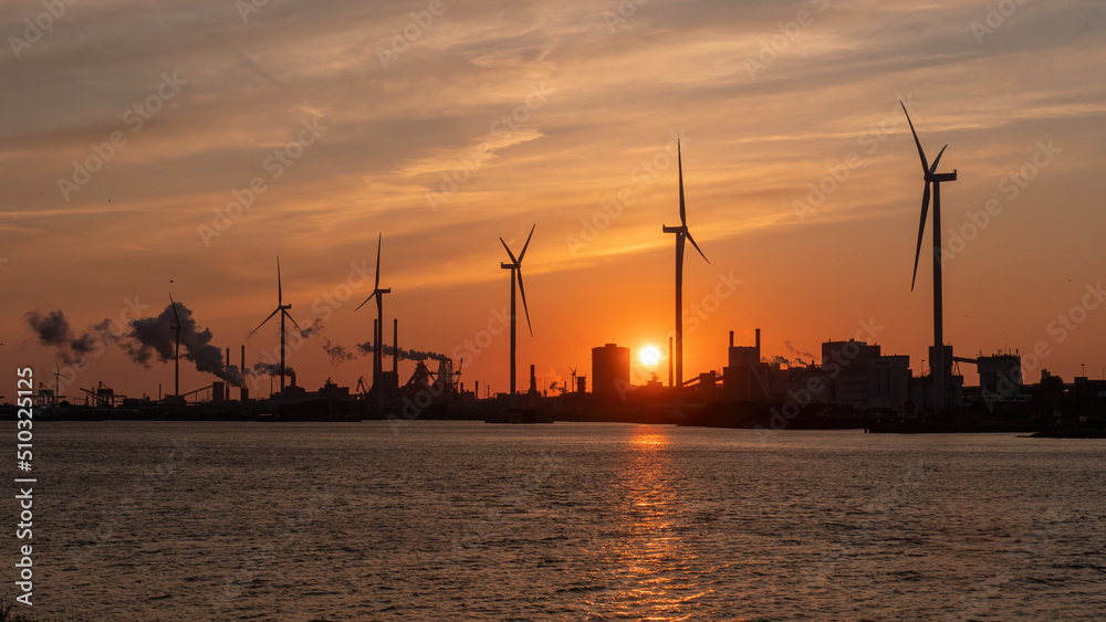Silhouette of wind turbines in industrial area by the sea on sunset