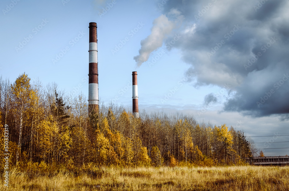 Red and white chimneys of the power plant exude smoke that mixes with low dark clouds