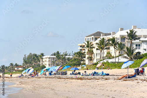 Tourists and locals with umbrellas on the beach with condos in the background at Lantana Beach in South Florida