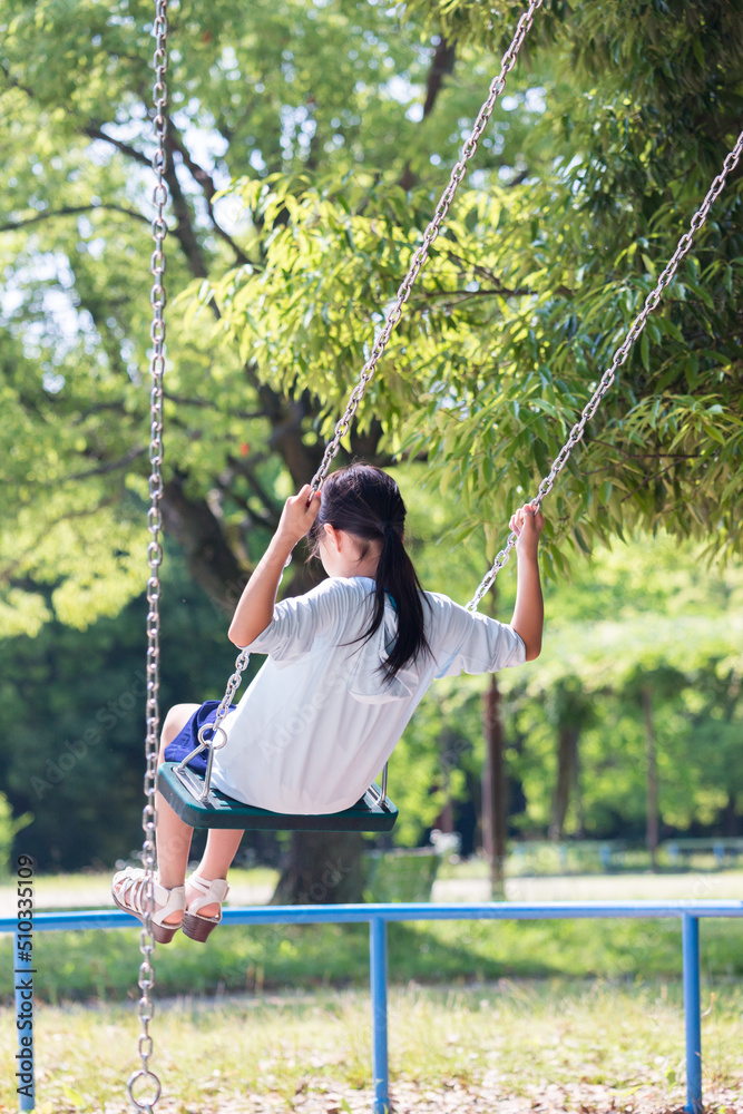 夏の公園でブランコを遊んでいる小学生の女の子の様子