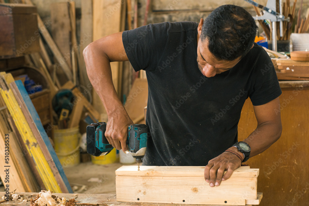 Latin American worker in his workshop using different tools. Wood craftsman creating pieces and polishing wooden parts. Local carpentry of the town and its operator doing some work.