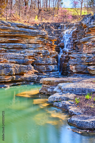 Fototapeta Naklejka Na Ścianę i Meble -  Teal waters show rocks next to jagged cliffs with waterfall