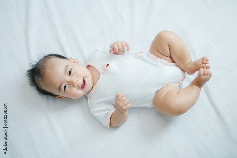 Cute little asian baby lying on white bed with soft blanket indoors Cute little asian baby lying on white bed with soft blanket indoors
