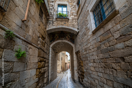 Fototapeta Naklejka Na Ścianę i Meble -  A small tunneled alley and back street of cobblestones in the medieval village of Girona Spain in the Catalonian district.