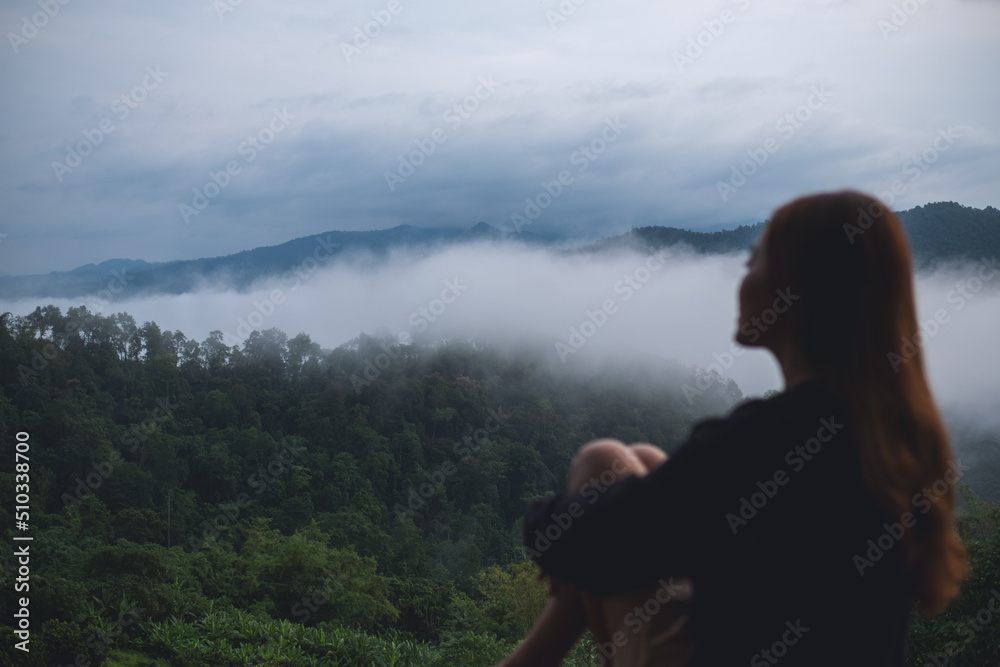 Blurred of a woman sitting on wooden balcony with a beautiful mountains and nature view on foggy day