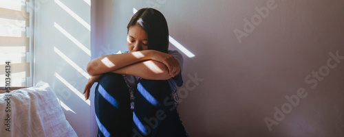 Asian women are sitting hugging their knees in bed. Feeling sad, disappointed in love In the dark bedroom and sunlight from the window through the blinds.