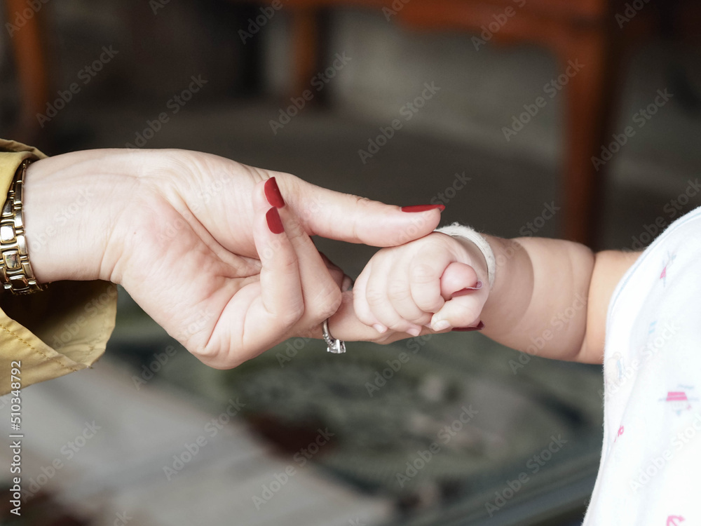 Closeup Shot of A Baby's Hand Holding Mother's Finger with Love.  Selective Focus and Blurred Background.