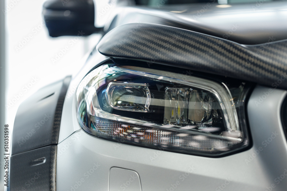 Close-up headlights of a modern silver color car. Detail on the front light of a car. Modern and expensive car concept. The car is in the showroom. Automotive concept. Classic silver color. LED light