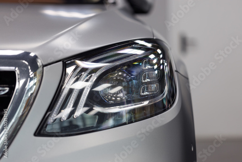 Close-up headlights of a modern silver color car. Detail on the front light of a car. Modern and expensive car concept. The car is in the showroom. Automotive concept. Classic silver color. LED light © svetlichniy_igor