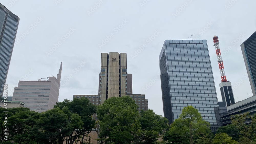 The Tokyo city buildings and offices peeking between the tree bushes of Hibiya Park, central downtown historic landmark that opened in 1903, shot taken on year 2022 June 11th

