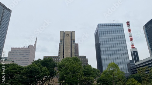 The Tokyo city buildings and offices peeking between the tree bushes of Hibiya Park  central downtown historic landmark that opened in 1903  shot taken on year 2022 June 11th 