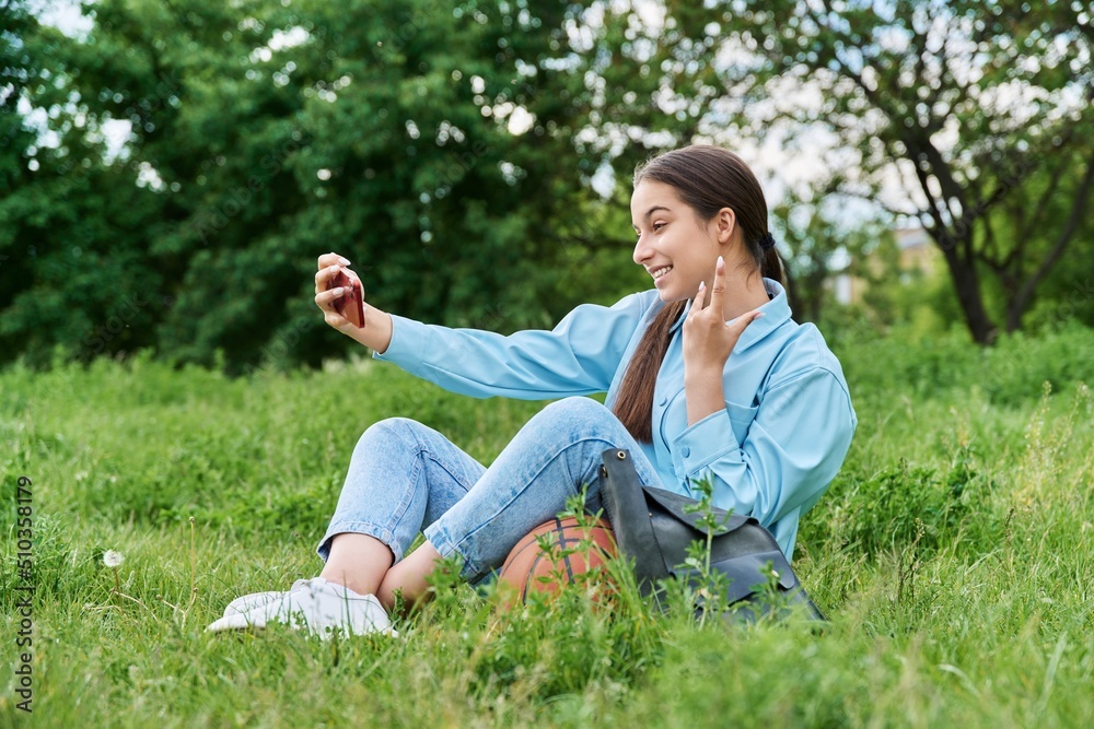 Fototapeta premium Teenage female student sitting on the grass using smartphone.