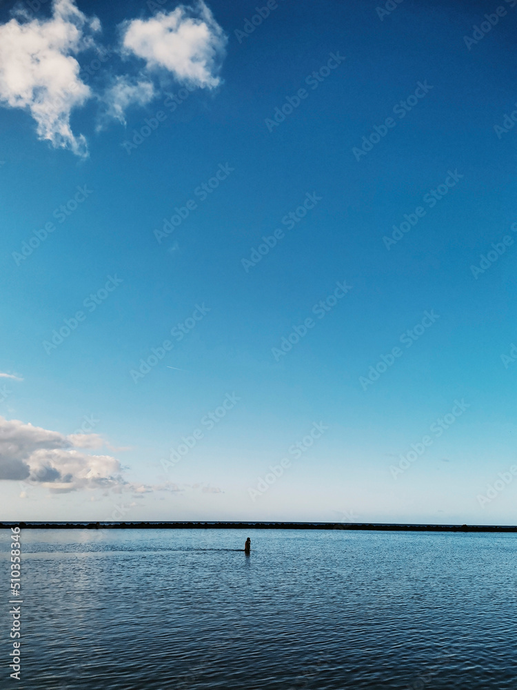Blue sea ocean water surface background. Concept of travel and summer holiday vacation in calm scenic place. Copy space and nature. Horizon and sky with clouds. People walking in the middle Blue sea ocean water surface background. Concept of travel and summer holiday vacation in calm scenic place. Copy space and nature. Horizon and sky with clouds. People walking in the middle