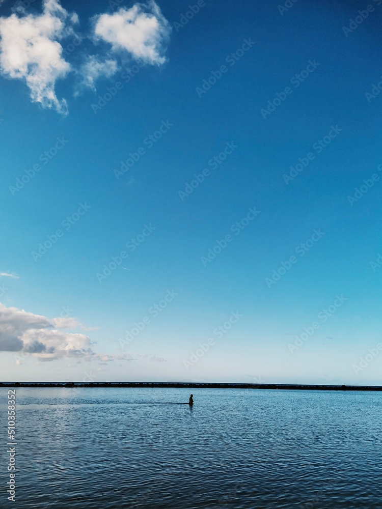 Obraz premium Blue sea ocean water surface background. Concept of travel and summer holiday vacation in calm scenic place. Copy space and nature. Horizon and sky with clouds. People walking in the middle