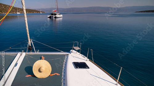 Beautiful young blond woman in bikini laying on catamaran bow at sunny summer day