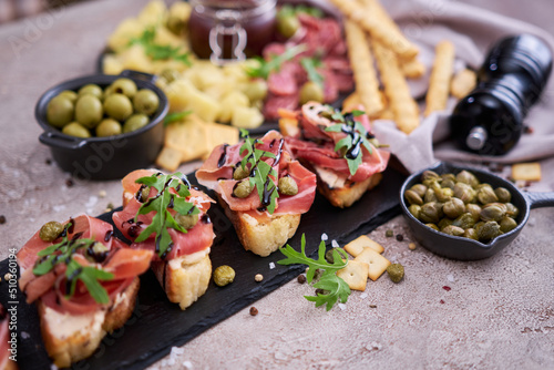 bruschetta with prosciutto ham and capers with traditional antipasto meat plate on background