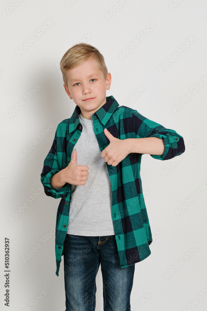 Portrait of cute stylish blond boy kid 7 years old in checked shirt and jeans showing thumb up, class Portrait of cute stylish blond boy kid 7 years old in checked shirt and jeans showing thumb up, class