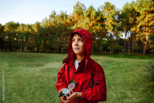 A boy in a red windbreaker against the backdrop of a forest with a compass in his hand.