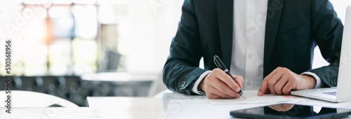 Cropped shot of businessman in suit writing business papers at desk in modern coworking office. copy space photo