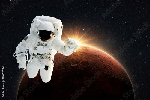 New spaceman flies in gravity in outer space on a backgrounds of the amazing red planet Mars with orange dawn rays in space. Astronaut Journey to the Planet Mars Concept