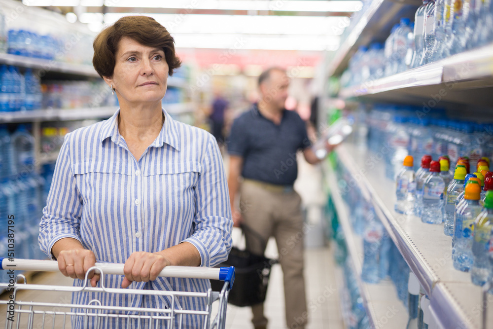 mature woman choosing bottle of drinking water in supermarket