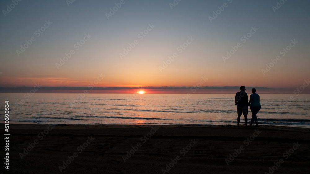 Two people, man and woman, watch the sunrise at the ocean