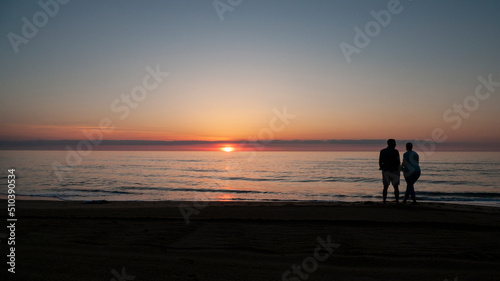 Two people, man and woman, watch the sunrise at the ocean